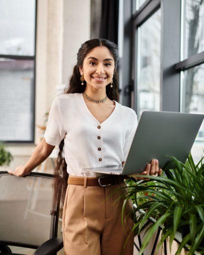 Lachende backoffice medewerker met een laptop, kijkend in de camera in een lichte kantooromgeving.